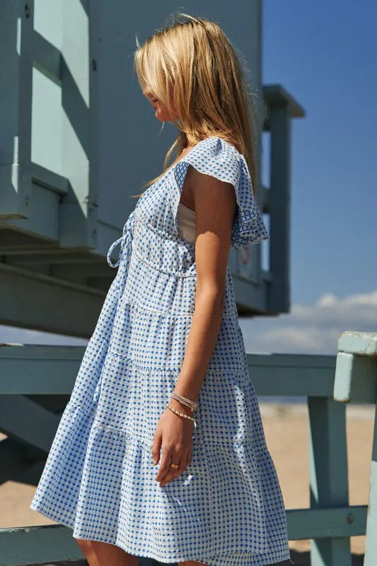  Close side view highlighting the cap sleeve cut and tiered panel detailing of this azure V-neck midi dress, offering a lightweight and breathable option for warm weather occasions.