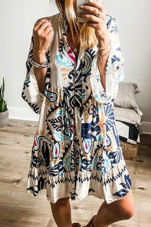  Model wearing a beige mini dress with a delicate all-over print and notched sleeves, styled with a relaxed silhouette for effortless charm.