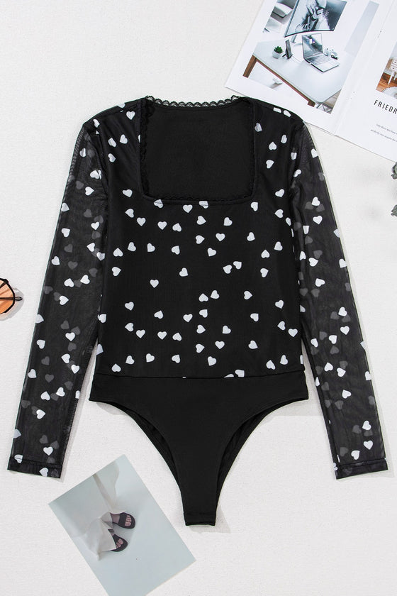 Laid-flat front image of the black bodysuit showing its intricate heart print mesh, clean neckline finish, and tailored structure for a secure yet feminine fit.

