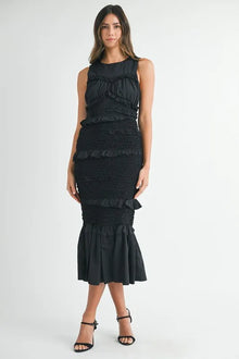  Full front view of the model wearing the black ruffled smocked midi dress, emphasizing its figure-hugging smocked bodice, romantic ruffle detailing, and gracefully flowing midi-length hem that flatters all body types.

