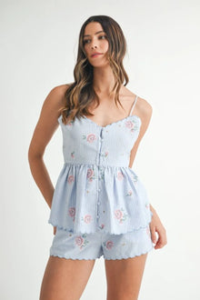  Woman wearing a blue peplum floral two-piece outfit, captured in a front view showcasing the scalloped neckline and delicate floral print.