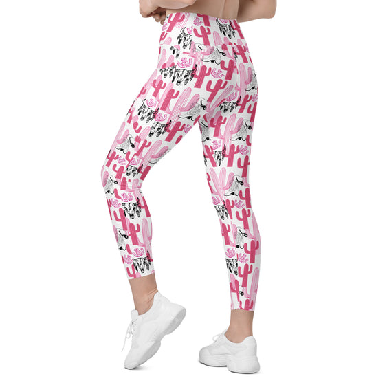 Model posing in high rise leggings with pockets. Cactus Cowgirl design in black with pink and white cactus print. Women's yoga pants with pocketed sides.