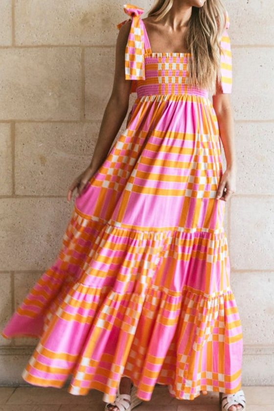 Woman wearing a vibrant Color Block Tie Shoulder Dress featuring pink and orange stripes, smocked bodice, adjustable ties, and a tiered maxi skirt.

