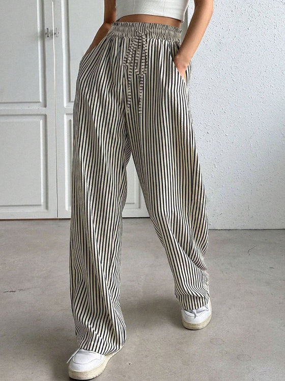 Woman wearing Drawstring Striped Elastic Waist Pants with a relaxed wide-leg fit, vertical stripes, elastic waistband, and functional side pockets, styled with a crop top and sneakers.