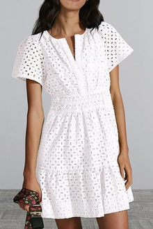  Woman wearing an Eyelet Notched Short Sleeve Mini Dress in white with intricate eyelet details, a notched neckline, and a flouncy mini hem