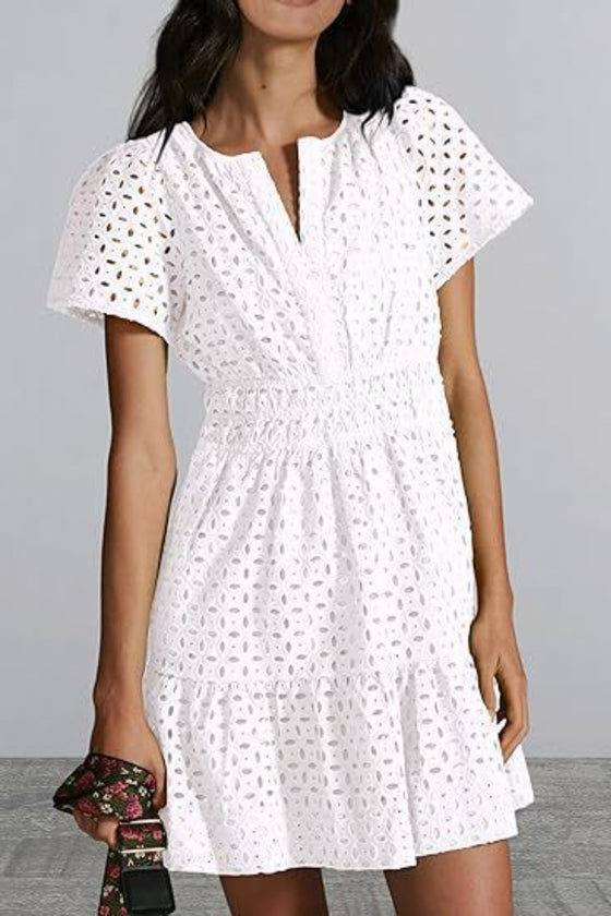 Woman wearing an Eyelet Notched Short Sleeve Mini Dress in white with intricate eyelet details, a notched neckline, and a flouncy mini hem