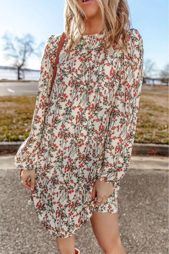 A woman wearing the Floral Round Neck Long Sleeve Mini Dress with a vibrant floral print, long sleeves, and a mini length, perfect for casual outings or gatherings.