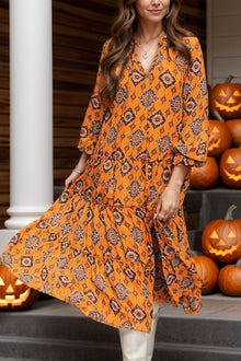  A woman wearing a vibrant orange printed maxi dress with a tie neck and frill hem, styled for a chic autumn look.