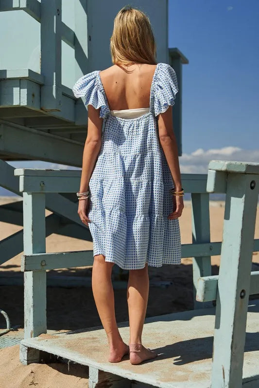 Full back view of the tiered dress in light azure shade, showcasing cap sleeves and an elegant drop to the hem, perfect for garden parties or a casual day out in the city.

