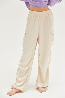  Woman wearing HYFVE Satin Drawstring Hem Cargo Pants in beige, featuring side flap pockets and adjustable drawstring hems for a chic yet functional style.

