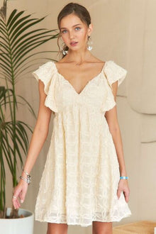  A timeless ivory mini dress featuring soft ruffled sleeves, a tiered silhouette, and a delicate tie-back detail, perfect for an elegant yet casual look.