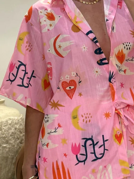 Front pose of a pink printed two-piece summer outfit showing soft tones, casual buttons, and matching printed skirt for feminine style.