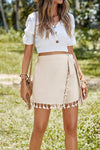 Model wearing a neutral beige wrap skirt with tassel trim and adjustable tie waist—styled for boho vibes, vacation looks, or sunny-day streetwear.