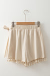 Back view of neutral beige wrap skirt displayed flat, highlighting adjustable tie waist and tassel detailing—perfect for laid-back seasonal dressing.