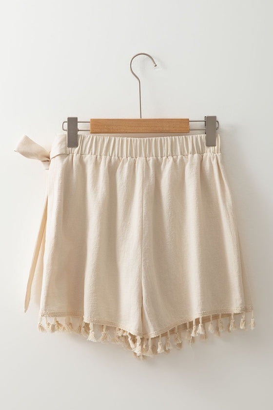 Back view of neutral beige wrap skirt displayed flat, highlighting adjustable tie waist and tassel detailing—perfect for laid-back seasonal dressing.