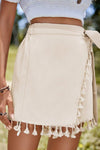  Front view of the tassel-trimmed neutral beige wrap skirt with a relaxed fit and tie waist—effortless for warm-weather style and beachwear.