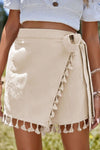 Close-up of neutral beige tassel-trimmed wrap skirt with tie waist, showcasing the soft fabric texture and stylish front detail—ideal for casual chic and boho summer looks.