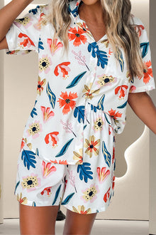  Woman wearing a vibrant floral printed button-up top and matching shorts, styled with pockets and a relaxed fit, perfect for casual summer outings.

