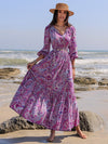 Woman wearing a paisley printed maxi dress with a tie neckline and balloon sleeves, perfect for beach outings and casual gatherings.

