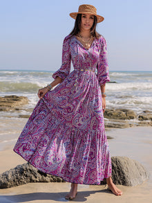  Woman wearing a paisley printed maxi dress with a tie neckline and balloon sleeves, perfect for beach outings and casual gatherings.

