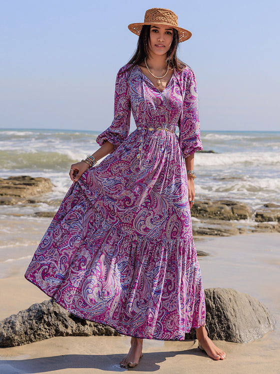 Woman wearing a paisley printed maxi dress with a tie neckline and balloon sleeves, perfect for beach outings and casual gatherings.

