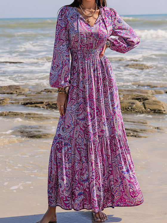 Woman styled in the Printed Tie Neck Maxi Dress at the beach, paired with a straw hat and accessories for a boho-chic look.