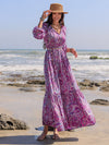 Woman styled in the Printed Tie Neck Maxi Dress at the beach, paired with a straw hat and accessories for a boho-chic look.