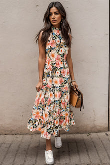  Woman wearing a floral midi dress with a mock neckline, tiered hem, and functional pockets, styled with a leather bag and white sneakers for a chic look.