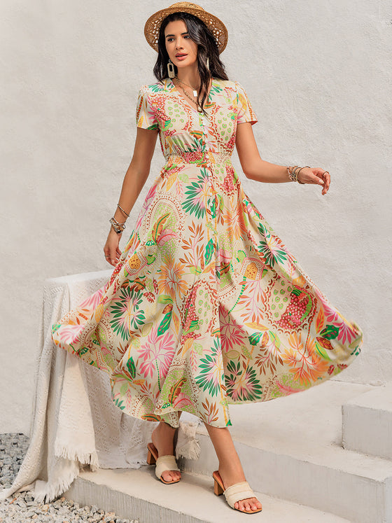 Woman wearing a Printed V-Neck Short Sleeve Midi Dress featuring a vibrant floral and paisley print, buttoned front, and practical pockets.