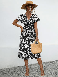  Full front view of the black V-neck dress featuring a subtle printed pattern, gently fitted waistline, and soft short sleeves that create a classic, streamlined silhouette.

