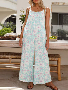  Woman wearing a pastel floral printed wide leg jumpsuit with adjustable tied straps and pockets, perfect for casual outings and beach days.