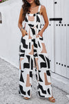 Woman wearing a navy blue wide-strap jumpsuit with an abstract white print, featuring a wide-leg design and side pockets, perfect for casual outings.