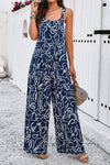 Woman wearing a navy blue wide-strap jumpsuit with an abstract white print, featuring a wide-leg design and side pockets, perfect for casual outings.