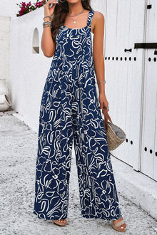  Woman wearing a navy blue wide-strap jumpsuit with an abstract white print, featuring a wide-leg design and side pockets, perfect for casual outings.