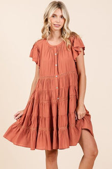  : A warm-toned midi dress featuring a tiered silhouette, delicate ruffle details, and a functional button-down front for effortless style.

