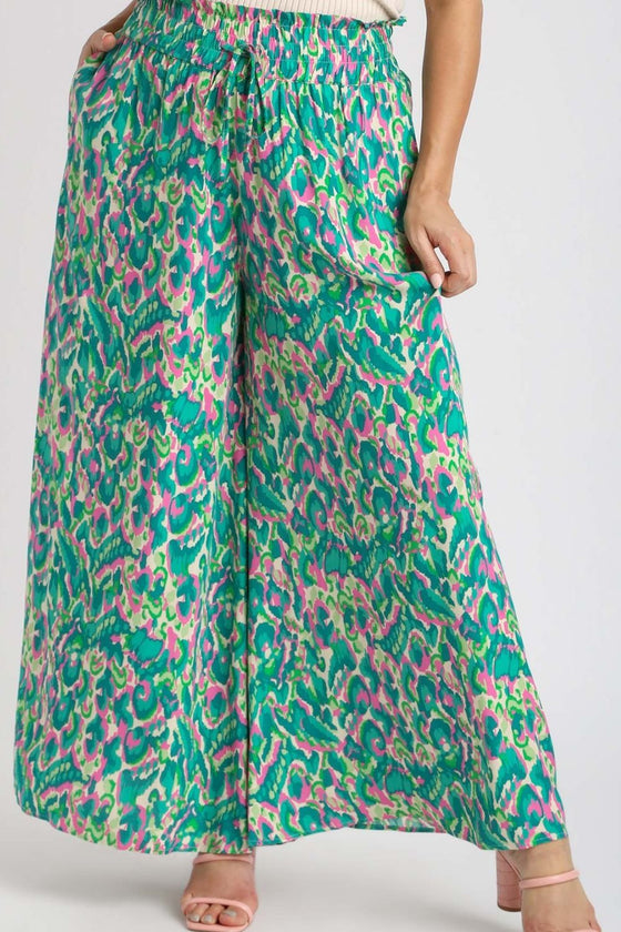 Model stands facing forward in the printed green pants, showing the fluid leg structure and high-waisted comfort fit.

