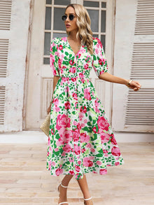  Woman wearing a Ruched Printed Surplice Short Sleeve Dress with a vibrant floral design, styled with white heels and sunglasses.