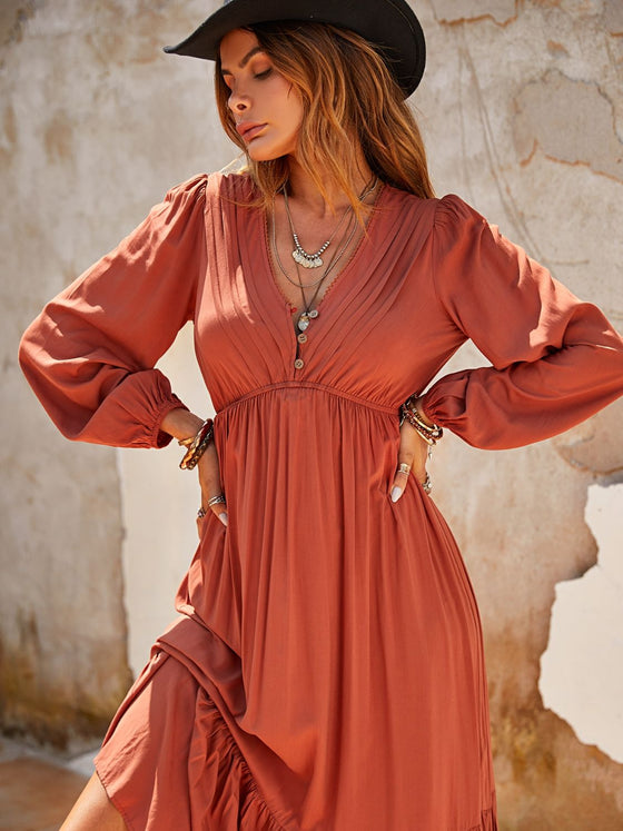 A woman wearing a Ruched V-Neck Long Sleeve Midi Dress with a ruffled hem, styled with boho jewelry and boots, perfect for casual or formal wear.

