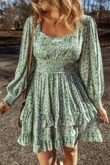  Model wearing a floral square neck dress with ruffle hem and long sleeves in a green and white floral print, styled for a casual outing.

