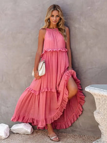  Woman wearing a sleeveless tiered maxi dress in pink, featuring ruffled layers, a high-low hem, and practical pockets. Styled for casual and elegant settings.