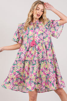  Woman wearing the SAGE + FIG Floral Ruffle Short Sleeve Dress featuring a floral print, tiered design, and playful tassels, perfect for summer outings.

