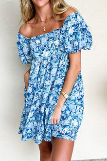  Model wearing the sky blue floral mini dress, standing with arms relaxed, showcasing the elegant puff sleeves, fitted waist, and charming floral print.

