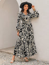 Woman styled in the Smocked Printed Tie Neck Maxi Dress, accessorized with gold jewelry, perfect for formal events.