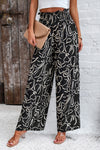 Woman in black Smocked Printed Wide Leg Pants with a modern print, designed with a comfortable smocked waistband.