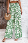 Woman wearing smocked green printed wide-leg pants with pockets in a bold, artistic pattern, perfect for casual and vacation wear.