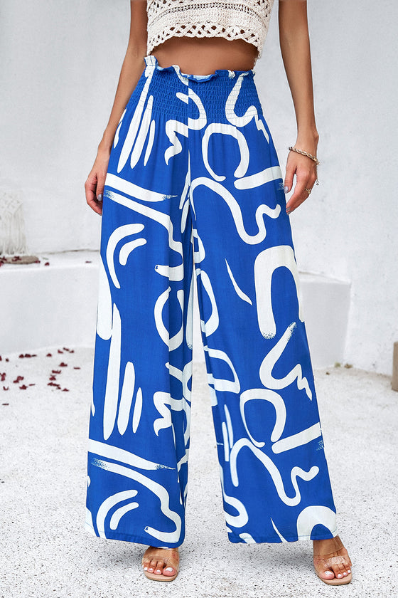 Main view woman wearing smocked printed wide-leg pants with pockets in a bold, artistic pattern, perfect for casual and vacation wear.