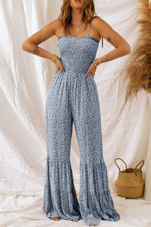  Woman wearing a Smocked Printed Wide Strap Jumpsuit with a floral print and wide-leg design, styled for a casual chic look.