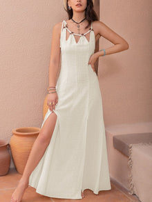  A woman wearing a Swiss Dot Cutout Sleeveless Maxi Dress in a soft white color, styled with statement jewelry, perfect for summer occasions.