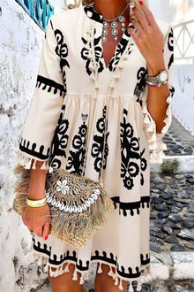  A woman wearing a Tassel Printed Three-Quarter Sleeve Mini Dress with a tied neckline, tassel detailing, and a boho-inspired black-and-white print.