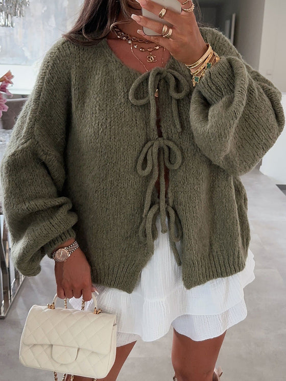 Woman wearing the cardigan in a cozy indoor setting, showcasing the tie closures and soft knit fabric.